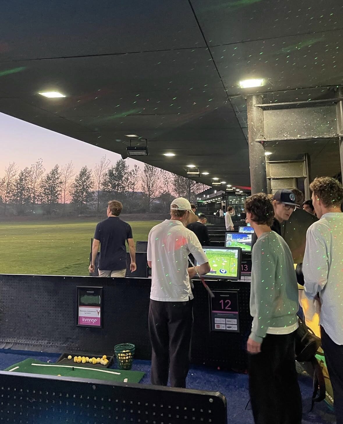 CBS Golf Academy members at a driving range at dusk